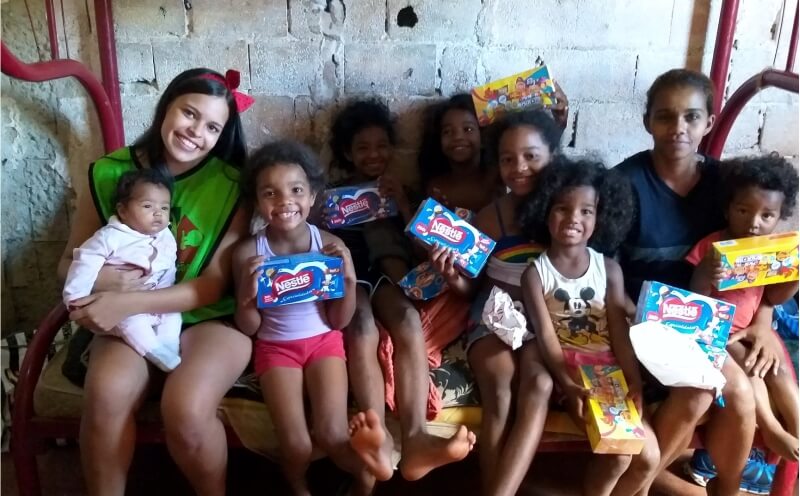 Voluntária e crianças comemorando a entrega de chocolates na Páscoa Solidária.